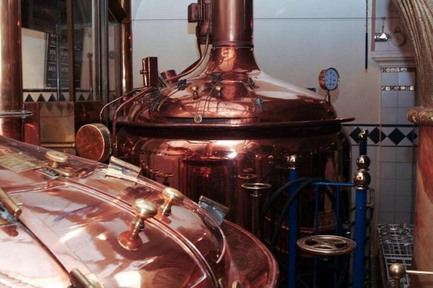 A copper distillation apparatus with a clock and a tiled wall in the background. 4