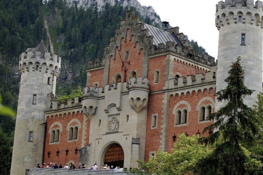 A castle with a large central tower, a red brick facade, and a mountainous backdrop. 2