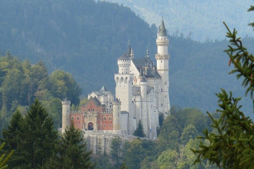 A castle with multiple towers and a red entrance, surrounded by trees and hills. 1