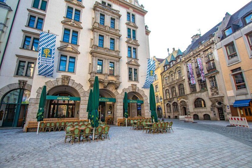 A historic building with arched entrances, outdoor seating, and flags. 1