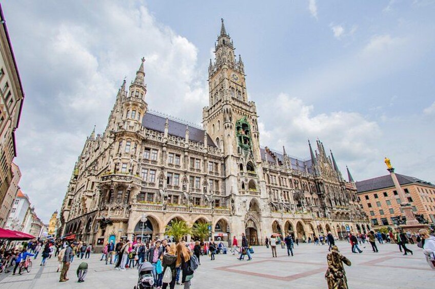 A historic building with intricate architecture, a large open square, and people walking around. 2