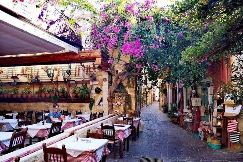 An outdoor café with tables and chairs, surrounded by potted plants and flowering vines. 1