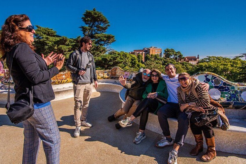 Un gruppo di persone sedute su una panchina in un parco, sullo sfondo alberi e edifici. 4
