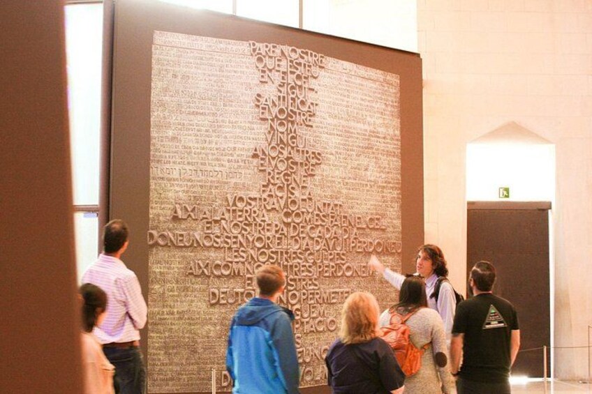 A large wall with engraved text, a person pointing at it, and several people observing. 5