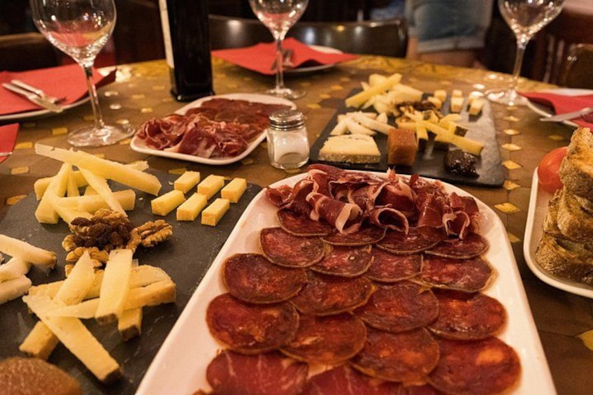Una tabla de embutidos con diversos quesos, carnes y galletas sobre una mesa. 2