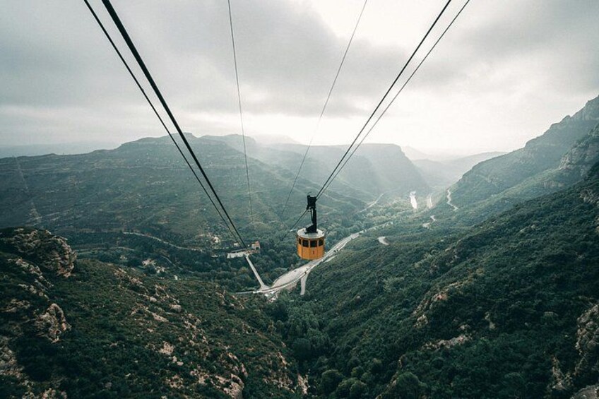 A cable car suspended over a mountainous landscape with a winding road below. 2