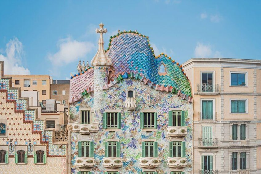 A colorful building with mosaic tiles, green shutters, and a unique roof design. 1