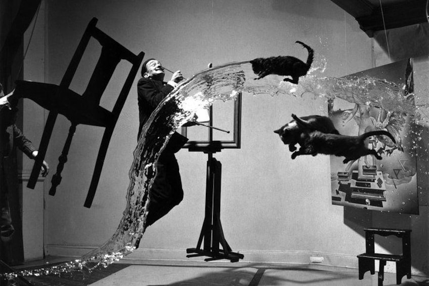 A person in a black suit with a chair and a cat in a room with a mirror. 3