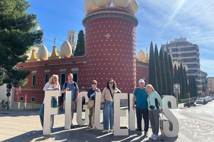 A group of people standing in front of a large red building with golden domes and a tall cylindrical structure with a cross on top. 5