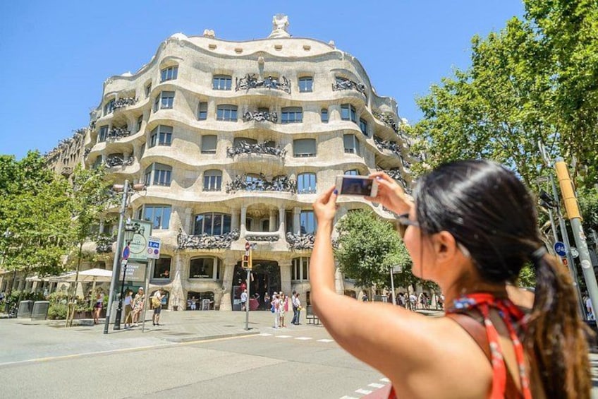 A woman taking a photo of a building with balconies and a unique architectural style. 1