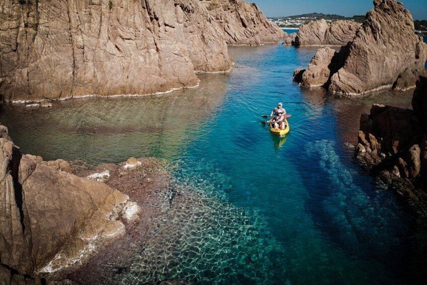 A person in a kayak navigating a clear blue waterway between rocky formations. 2