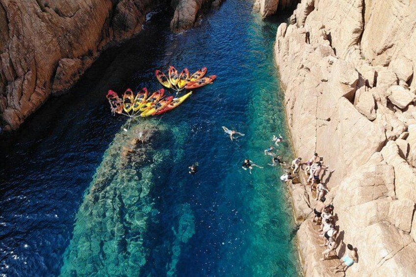 A group of kayaks on a river, people swimming, and a rocky cliff. 4