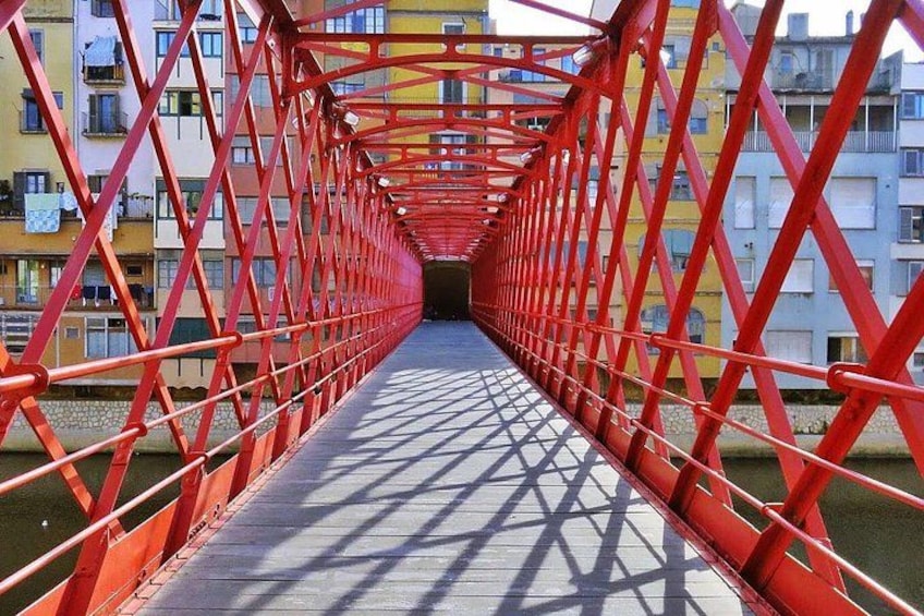 A red metal bridge with a walkway, surrounded by buildings. 4