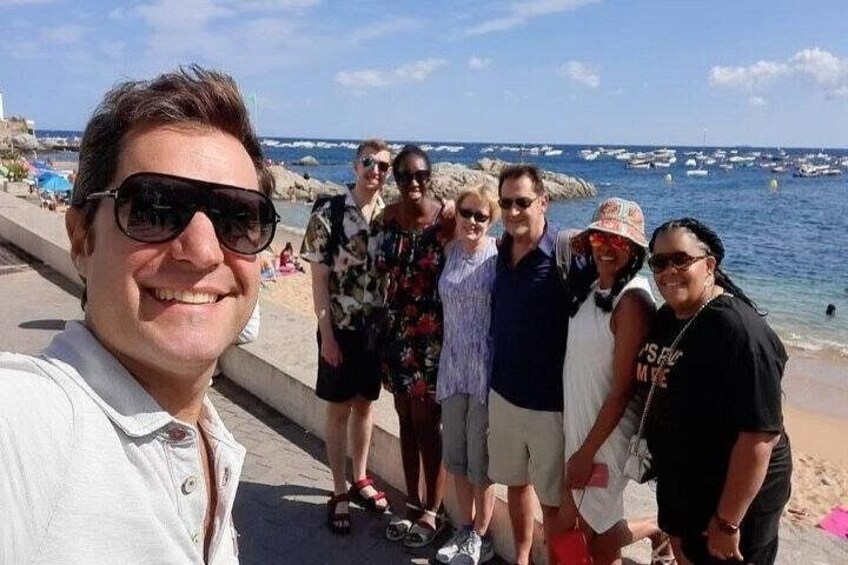 A group of people standing on a beach with the ocean and boats in the background. 3