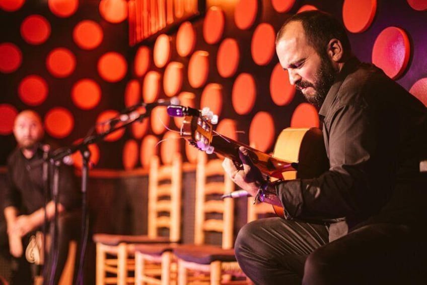 Una persona suona una chitarra acustica su un palco illuminato da luci rosse. 1