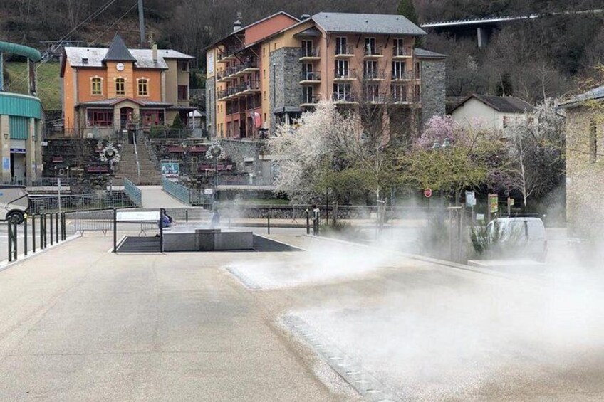 A fountain with water spray, a building with a red roof, and a staircase leading up to it. 3