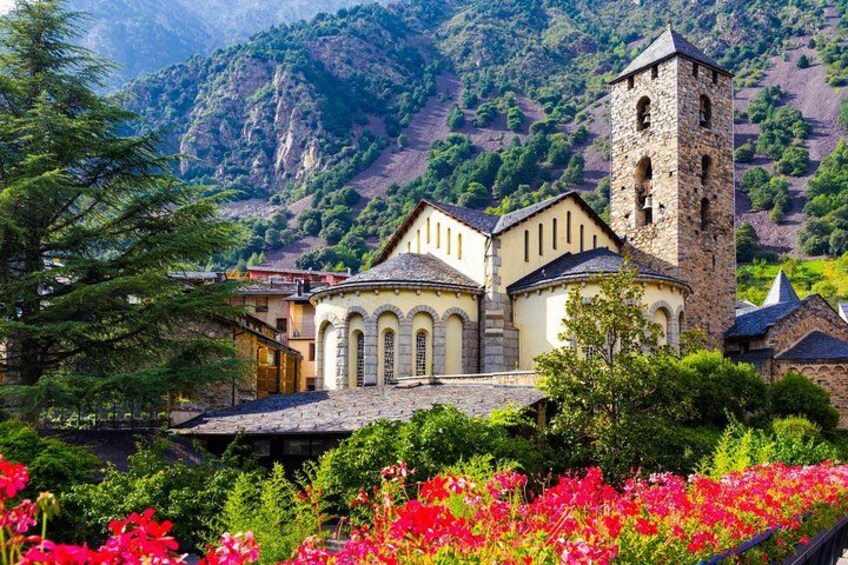 A church with a bell tower, surrounded by lush greenery and flowering plants. 1