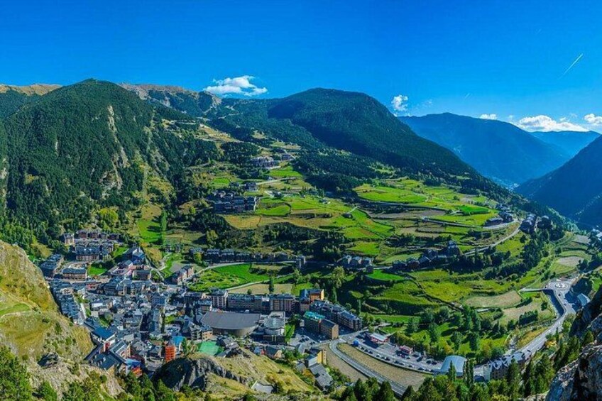 A mountainous landscape with a town nestled in a valley, surrounded by green fields and forested hills. 2