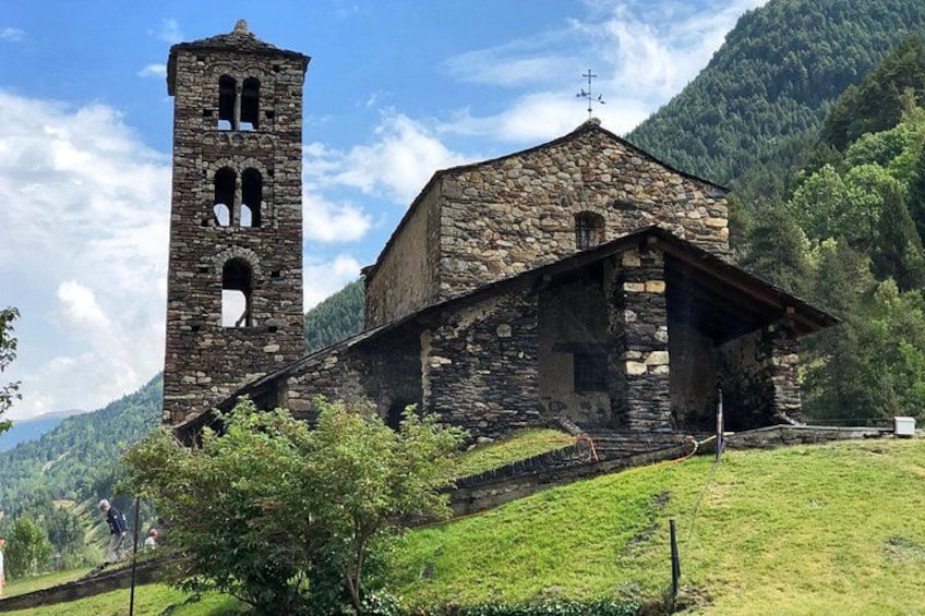 A stone church with a bell tower, surrounded by lush green hills and a clear sky. 2