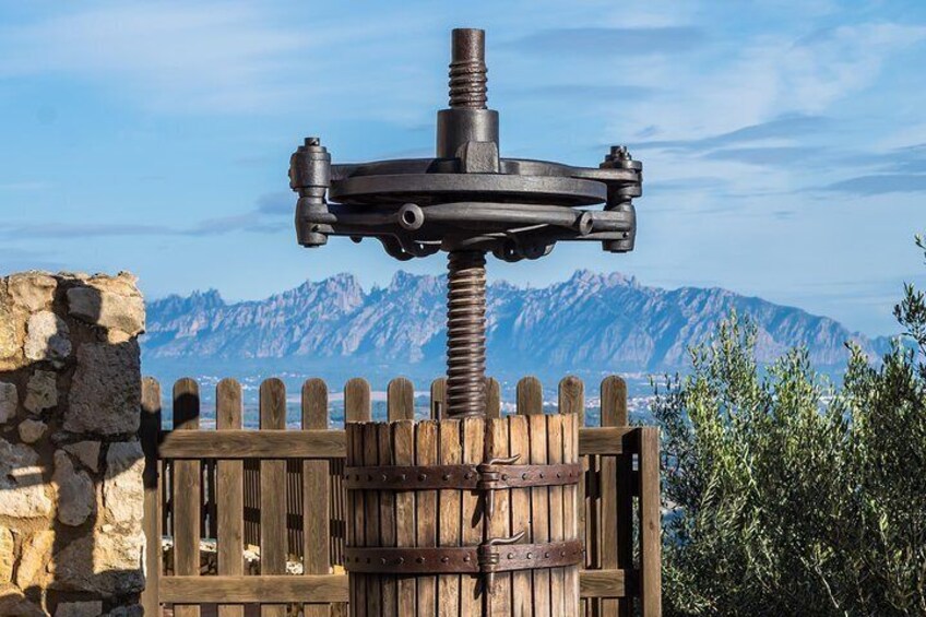 A wooden barrel with a metal spigot, set against a stone wall and wooden fence, with a mountainous backdrop. 3