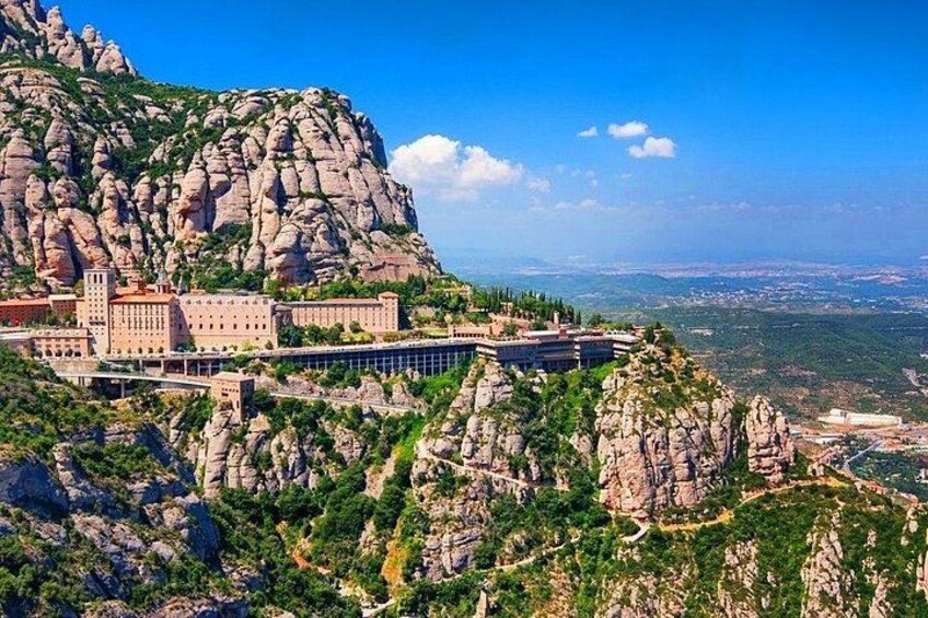 A mountainous landscape with a large building complex on a cliff, surrounded by rocky terrain and greenery. 5