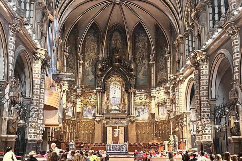 An ornate church interior with high vaulted ceilings, detailed stonework, and a central altar. 2