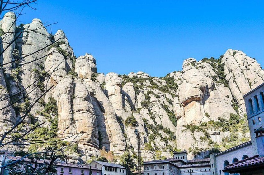 A rocky mountain with a clear sky, a building with arches, and a tree in the foreground. 2