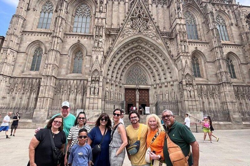 Un grupo de personas frente a una catedral grande y ornamentada con intrincados detalles de piedra y una entrada arqueada destacada. 5