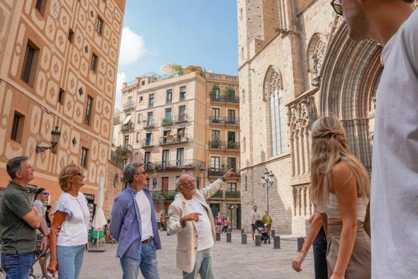 A group of people in a square with historical buildings, one with a pointed arch. 2