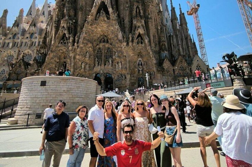 Un groupe de personnes posant devant une cathédrale historique, ornée de sculptures complexes en pierre, avec une grande structure circulaire sur le côté gauche. 2
