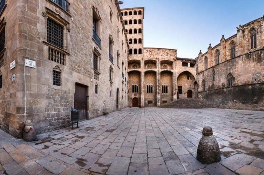 A historic courtyard with stone buildings, a central fountain, and a clear sky. 3