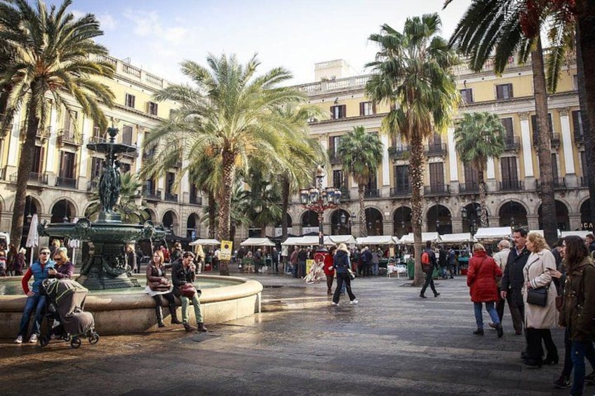 A bustling public square with palm trees, a fountain, and historic buildings. 2