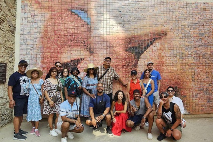 A group of people posing in front of a large mosaic mural. 3