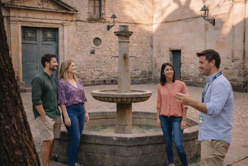 A group of people standing around a fountain in an outdoor setting with stone buildings in the background. 3
