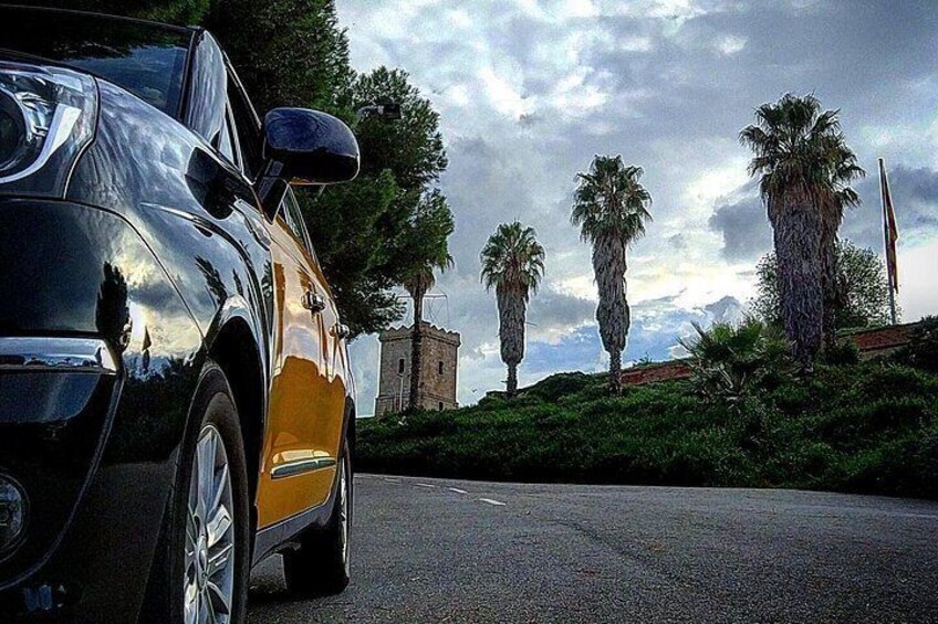A black convertible car parked on a road with palm trees and a stone tower in the background. 2