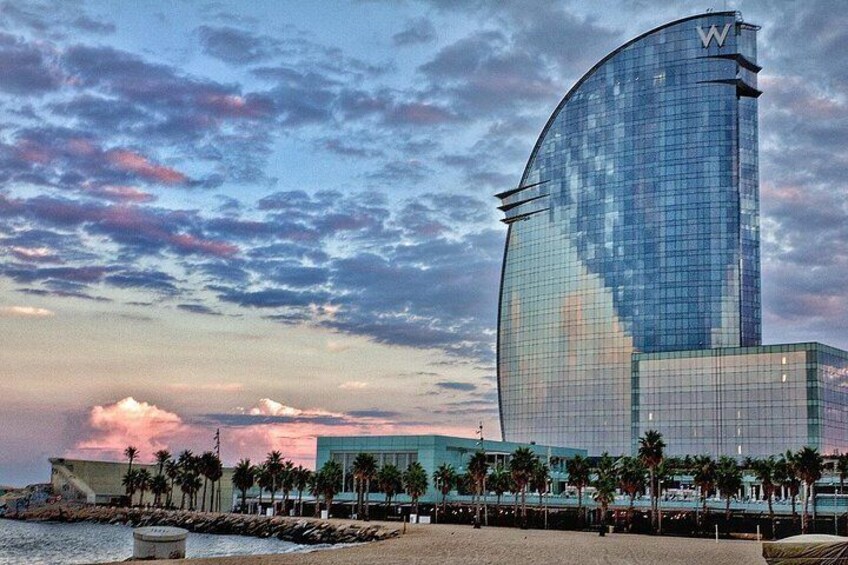 A modern building with a curved glass facade, palm trees, and a waterfront. 4