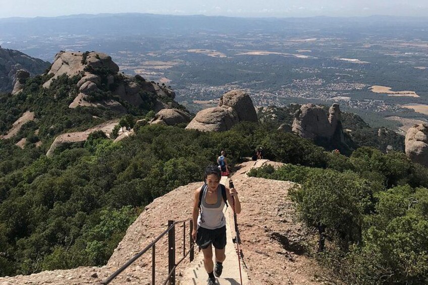 A person walking on a rocky trail with a scenic view of a town and mountains in the background. 2