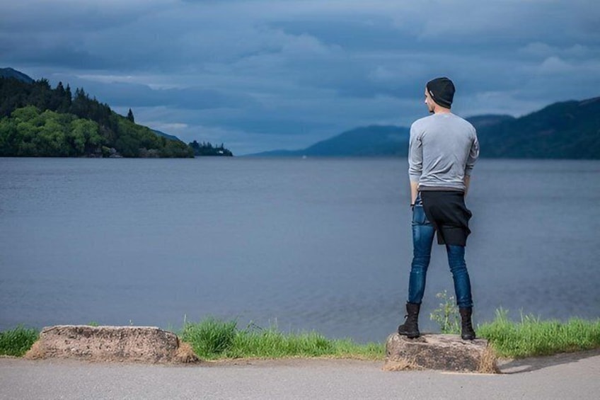 A person standing on a rock by a lake, with mountains in the background. 1