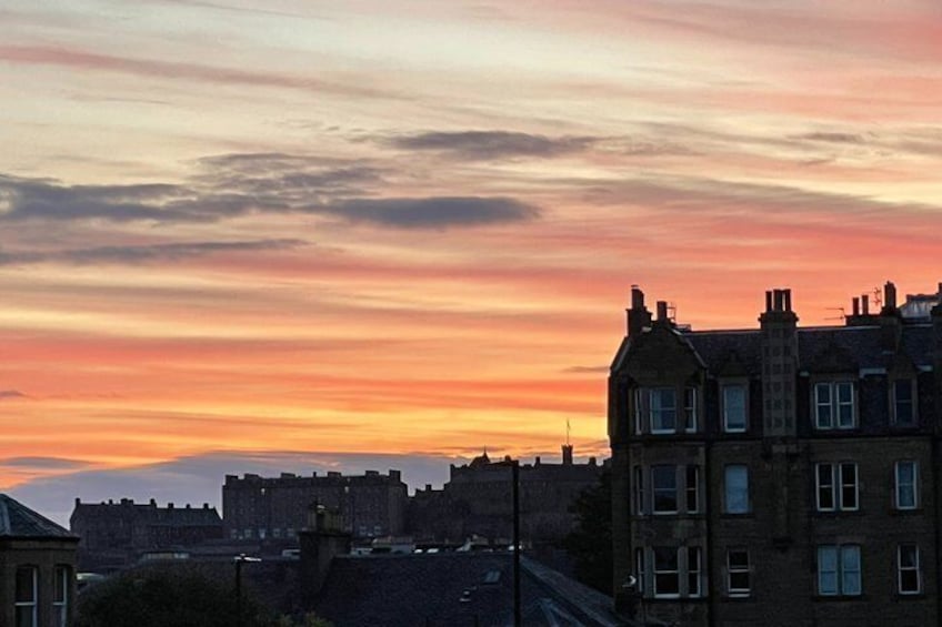 Ein Sonnenuntergang über einer Stadtlandschaft, Gebäude zeichnen sich vor einem farbenprächtigen Himmel ab. 3