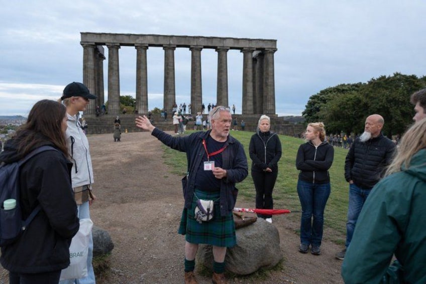 A group of people standing in front of a large stone structure with columns, possibly a historical monument. 1