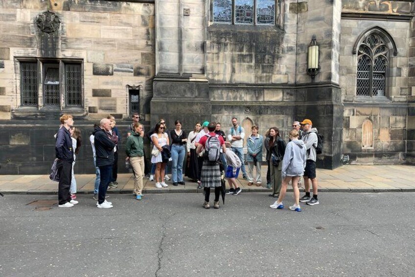 Eine Gruppe von Menschen steht auf einer Straße vor einem historischen Gebäude mit Steinarchitektur. 4