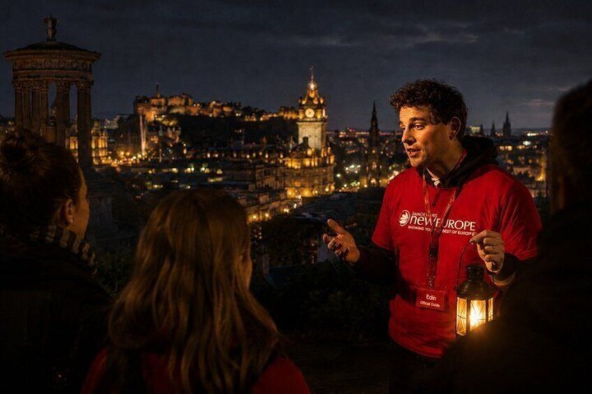 A person in a red shirt with 'NEW EUROPE' text, standing and gesturing, with a cityscape in the background. 1