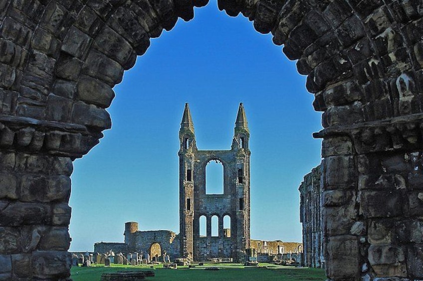 A historic stone archway framing a ruined church with a tall bell tower. 2