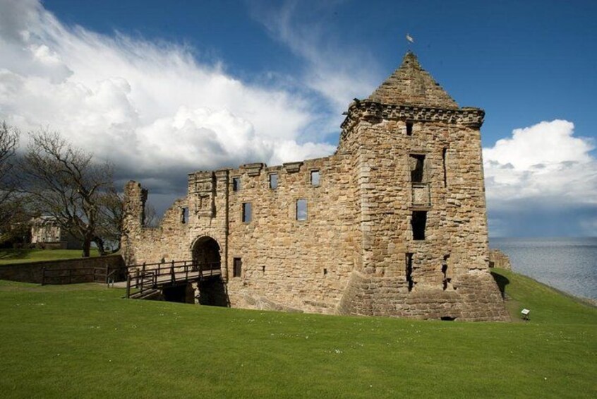 Un château en pierre doté d’une tour, avec un premier plan verdoyant et une étendue d’eau en arrière-plan. 4