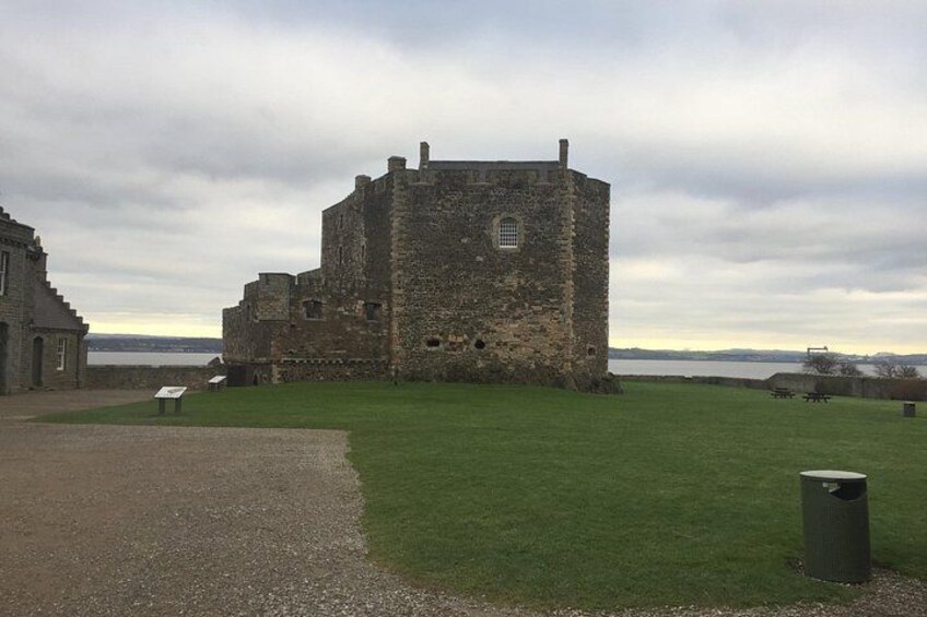 Un castillo de piedra histórico con un patio cubierto de césped y una masa de agua al fondo. 2