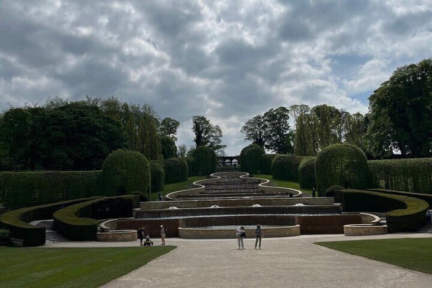 A formal garden with a central pathway, neatly trimmed hedges, and a distant view of a building. 2