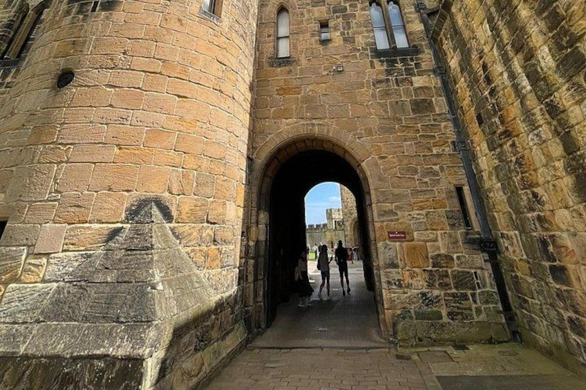 A stone archway leading into a historic building with tourists walking through. 2