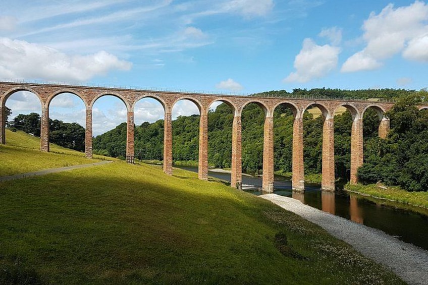 A brick viaduct with multiple arches spanning a river, surrounded by green grass and trees. 3