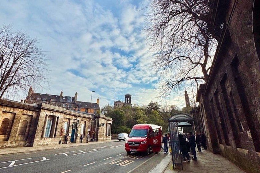 A street with a red bus, a bus stop, and historic buildings. 2