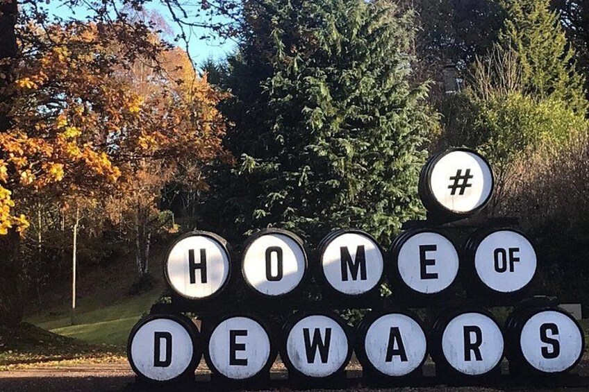 Une enseigne portant l'inscription « DEWARS, ICI EST SA MAISON », entourée d'arbres et de feuilles d'automne. 3